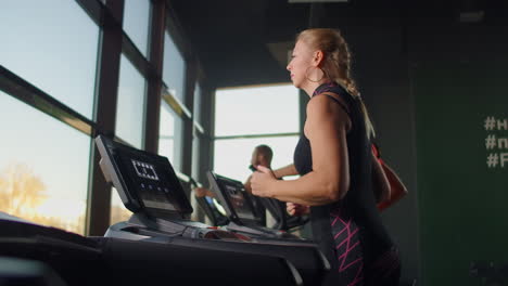 a group of people running on treadmills near a large panoramic window. group cardio workout