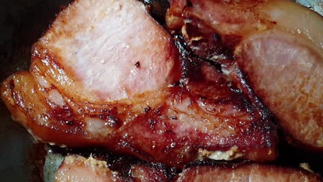 slow motion pan of pork chops meat in cast iron frying pan with olive oil for food presentations, almost done and ready to be served.