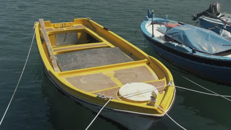 Pequeño-Barco-De-Lago-De-Plástico-Amarillo-Brillante-Amarrado-En-El-Puerto-Costero-Paneles-De-Madera-Contrachapada-A-Cámara-Lenta