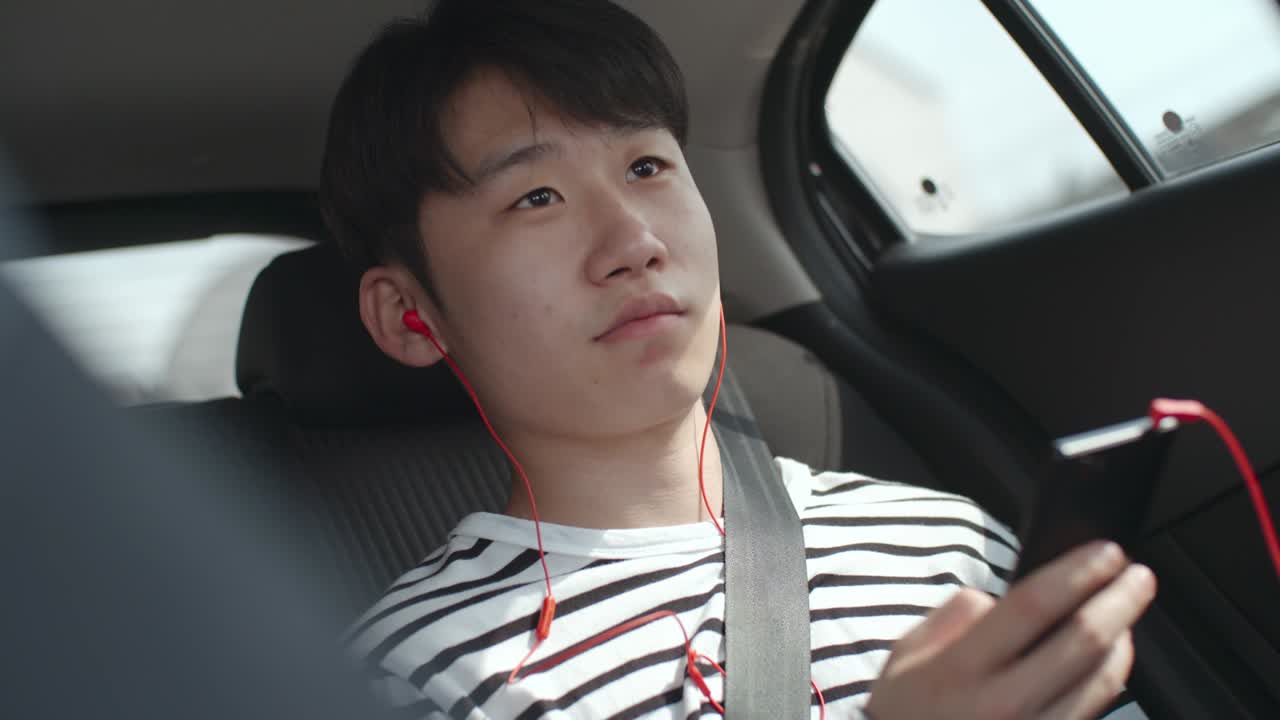 아시아 젊은이가 음악을 듣고 스마트폰으로 타이핑하고 있습니다.