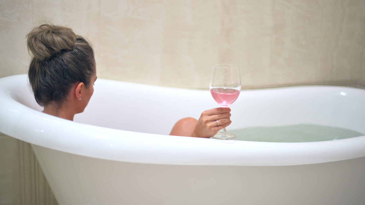 Woman relaxing in the bathtub, drinking rose wine