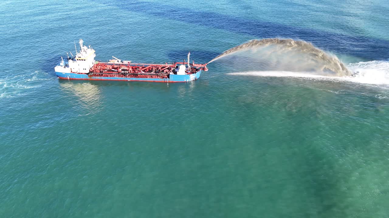 A dredging vessel sprays sand into the ocean near Gold Coast, Australia, under clear skies with calm waters