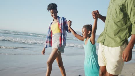 happy african american couple walking with daughter on sunny beach