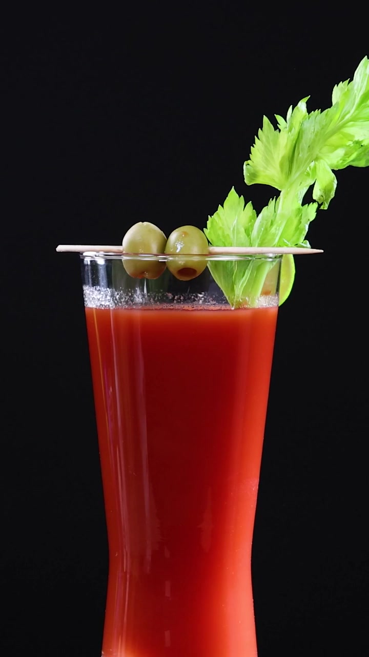 Um vibrante coquetel de suco de tomate vermelho guarnecido com aipo, limão e azeitonas contra um fundo preto.
