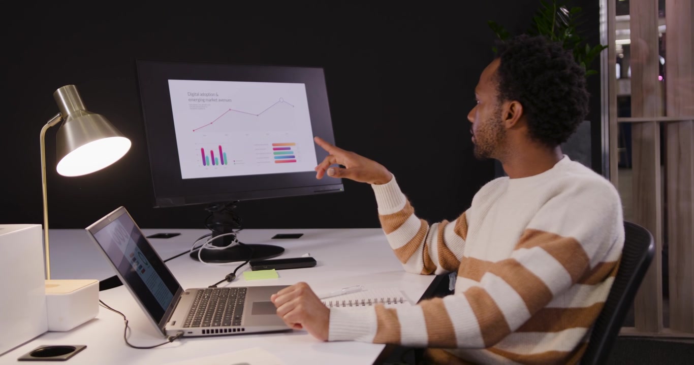 African American man typing on laptop, viewing monitor charts, pointing, analyzing, copy space