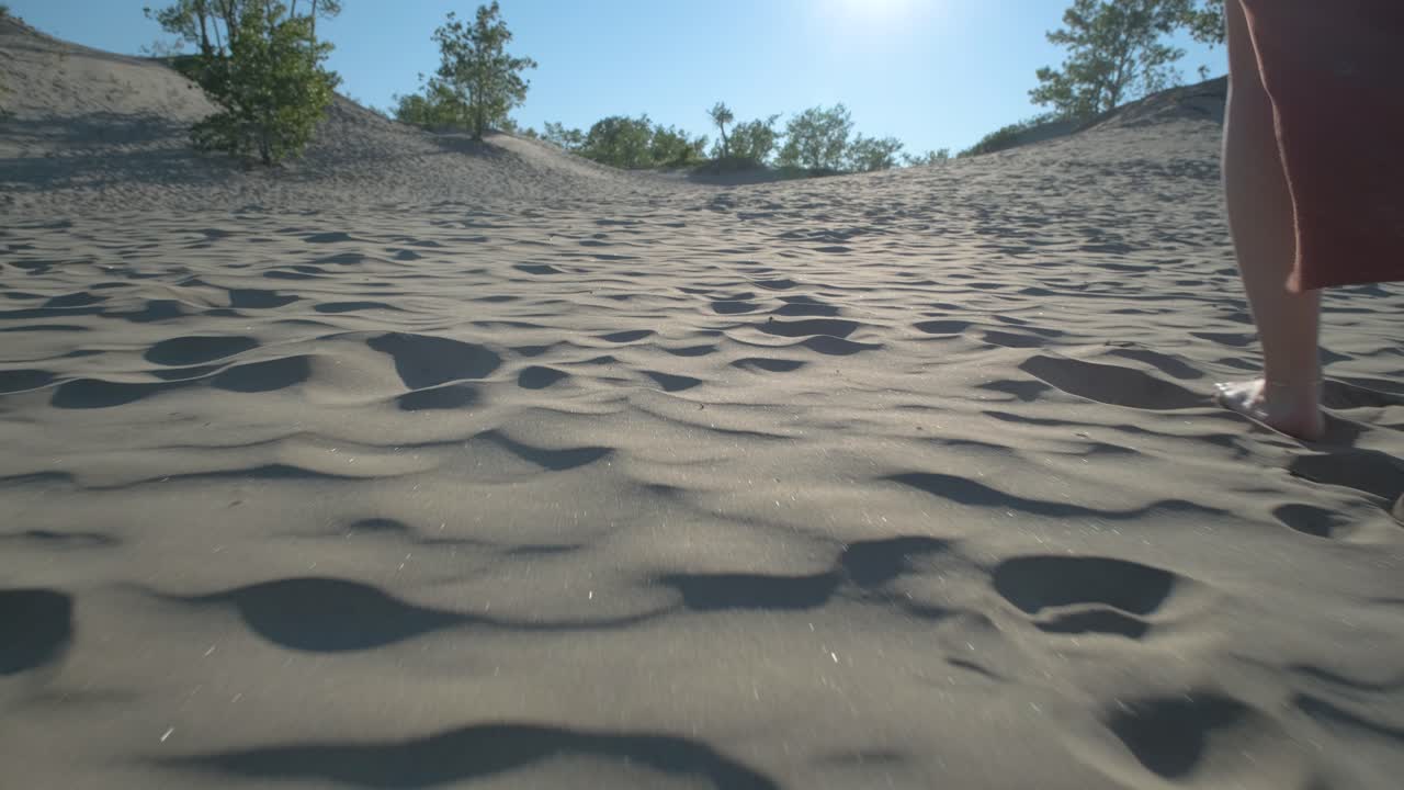 Woman walking barefoot in the sand towards the sunset