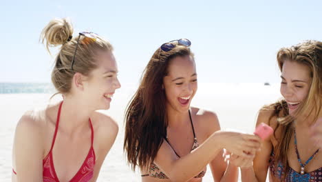 Three-teenage-girl-friends-taking-selfie-on-beach-wearing-colorful-bikini-sharing-vacation-photo