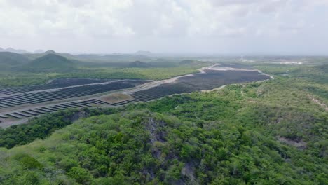 Ascending-drone-shot-of-large-solar-panel-power-station-park-with-green-scenery-during-cloudy-day