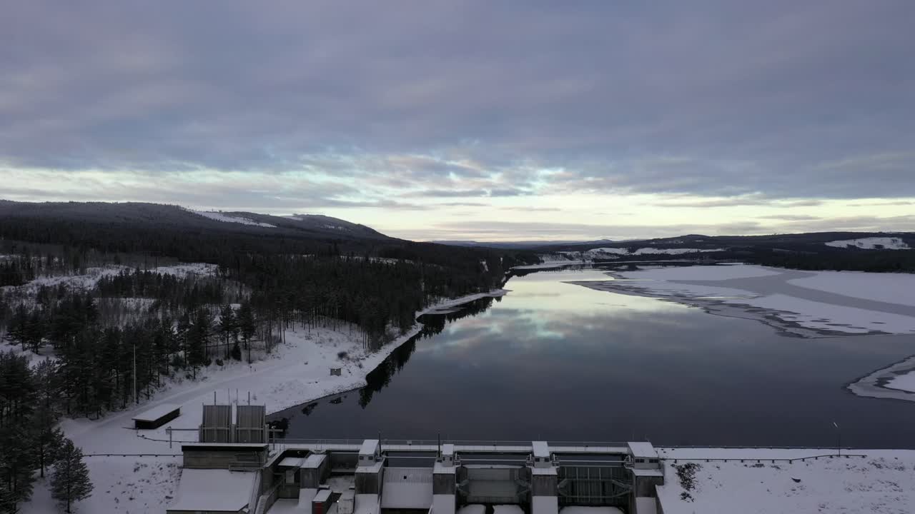 Unenomainen peruutuskamera ilmakuva järven peilikuvasta, paljastaen padon, metsäisen talvimaiseman, Asendammen, Ruotsi