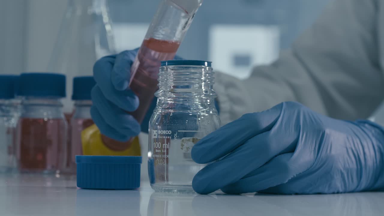 Lab worker's hand pouring red serum liquid into bottle while working in Medical Drug Production