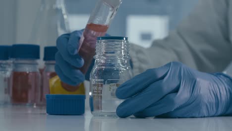 lab worker's hand pouring red serum liquid into bottle while working in medical drug production