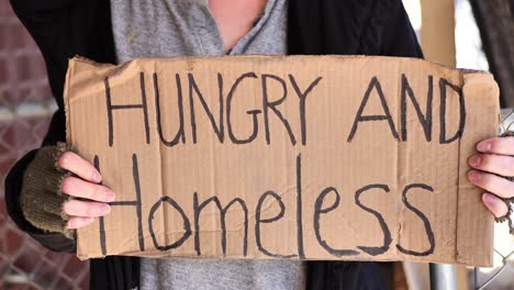 Close-up-handheld-shot-of-homeless-women-holding-sign-saying,-"Hungry-and-Homeless"