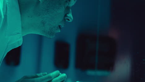 man washing face in a teal-lit room