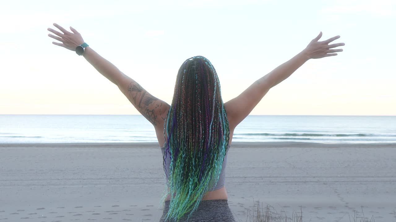 mujer con trenzas respira y extiende los brazos en la playa al amanecer