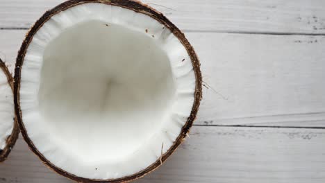 two halves of a coconut on a white wooden surface