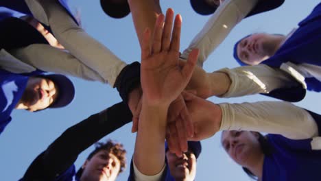 low angle view of diverse group of female baseball players making hand stack against blue sky