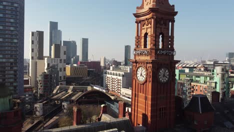 Vuelo-Aéreo-De-Drones-Sobre-El-Edificio-Del-Refugio-En-El-Centro-De-La-Ciudad-De-Manchester-Volando-Más-Allá-De-La-Torre-Del-Reloj-Y-Elevándose-Para-Dar-Una-Vista-De-Los-Rascacielos-Y-Tejados-En-La-Distancia