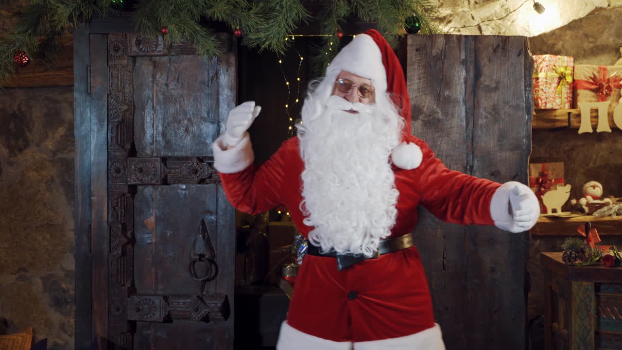 Half-length portrait of Santa in red suit near the wooden door. Santa Claus with long white beard invites to his residence by arm gesture.