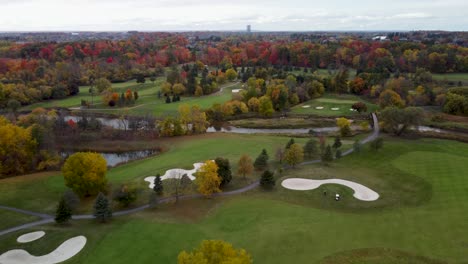 fly over a golf course surrounded by a park in a fall, cloudy, moody day