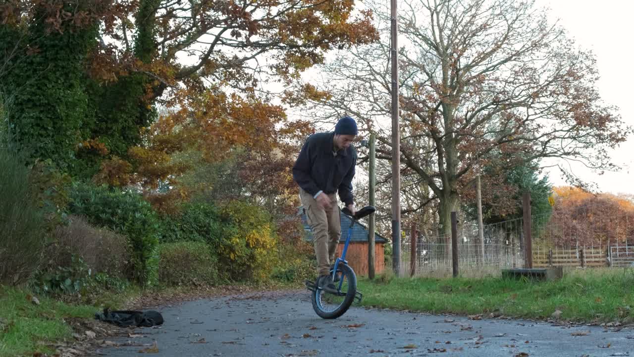 Man riding unicycle, practicing tricks outdoors in autumn, with leaves scattered around