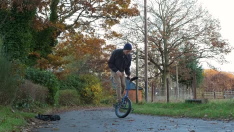 man riding unicycle, practicing tricks outdoors in autumn, with leaves scattered around