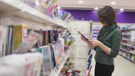 portrait of beautiful caucasian woman standing in magazine department in the supermarket and looking through magazines