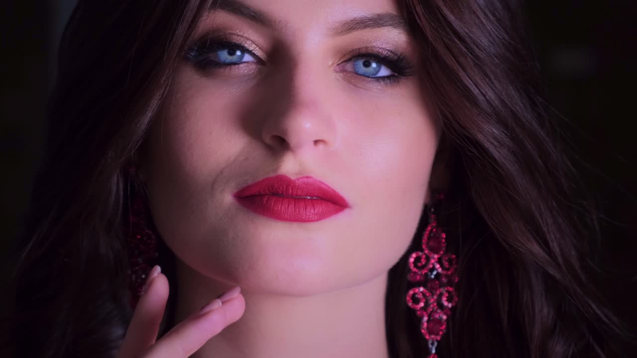 Striking Close-Up of a Woman with Captivating Blue Eyes and Bold Red Lips, Exuding Confidence and Charm with Elegant Earrings Highlighting Her Features