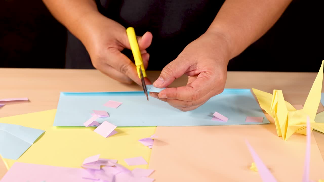 Person cuts pastel paper squares for origami, well-lit tabletop, close-up, steady camera
