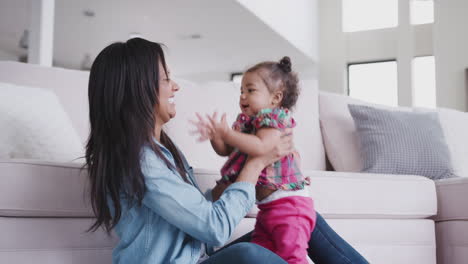 Mother-Playing-With-Baby-Daughter-Lifting-Her-In-The-Air-At-Home