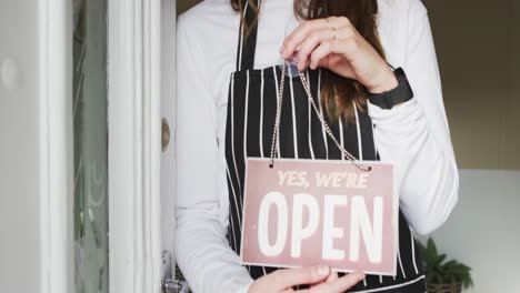 Midsection-of-young-caucasian-waitress-standing-in-door,-holding-open-sign