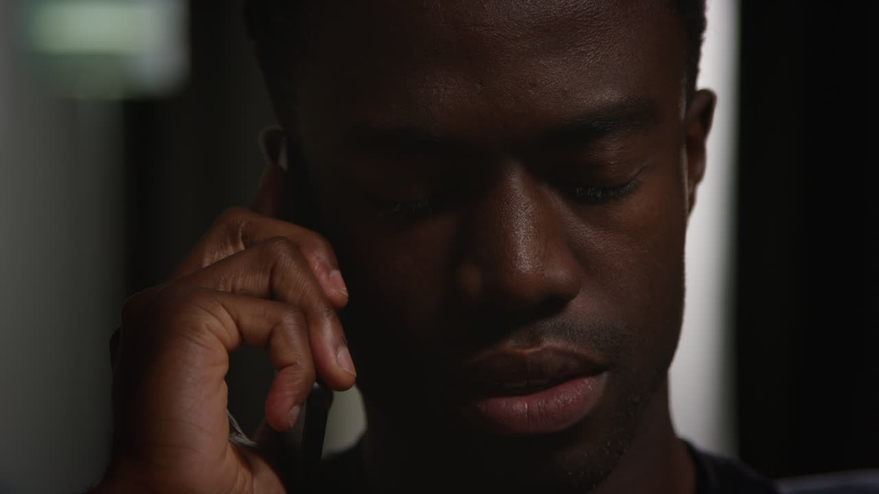 Close Up Of Unhappy And Depressed Young Man Sitting On Sofa At Home Making Call On Mobile Phone At Night