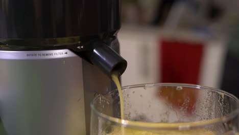 close up of electric juicer in use with nozzle pouring healthy fruit juice into glass pitcher - making healthy fresh fruit juice with selective focus on electric juicer kitchen appliance