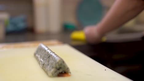 un cocinero corta el rollo de sushi en forma de triángulo en pequeños trozos iguales y limpia su cuchillo con una servilleta de cocina después de cada corte