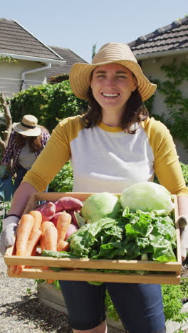 video vertical de una mujer caucásica sonriente en un jardín soleado llevando verduras recién recogidas