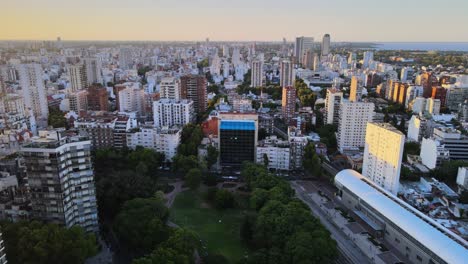 dolly out flying over barrancas de belgrano park and train station surrounded by buildings at sunset, buenos aires, argentina