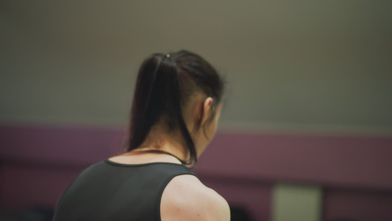 asian woman in gym preparing for heavy set, closeup back and shoulders, black tank top, ponytail, soft cinematic lighting, introspective mood, deliberate warmup, focused breathing, quiet dedication