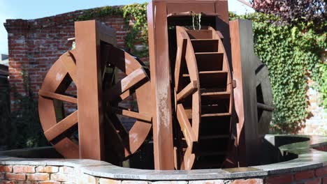 wooden watermill working. rolling wheels of water mill in sunny daytime, red brick wall