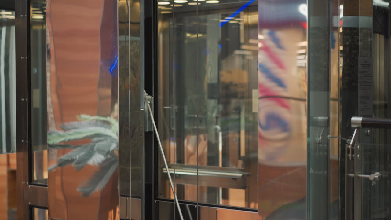 쇼핑몰에서 움직이는 현대적인 유리 엘리베이터, 우아한 반사, 기계적 세부 사항, 그리고 주변 인테리어와 광고에서 흐릿한 생생한 색을 보여줍니다.