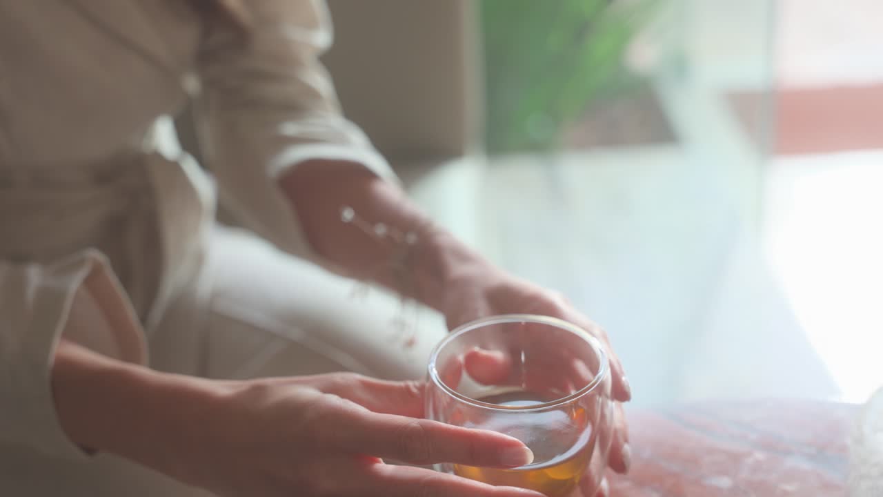 Una donna tiene in mano un bicchiere di tè. Il bicchiere è mezzo pieno e la donna si sta godendo la sua bevanda. Concetto di relax e comfort, dato che la donna è seduta a un tavolo di legno