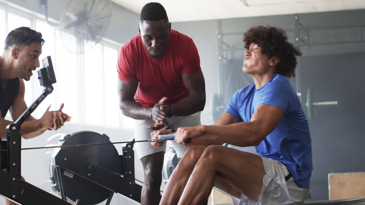 Group of diverse young men training in gym with rowing machine