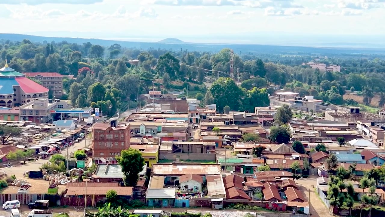 A cinematic view of rural Kenya showcasing informal settlements with rusted tin roofs, weathered homes, dusty village paths, and everyday community life.
