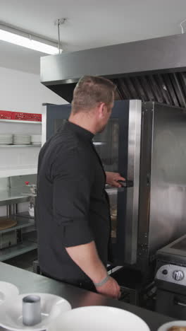 caucasian male chef closing oven doors and crossing arms in kitchen, slow motion, vertical