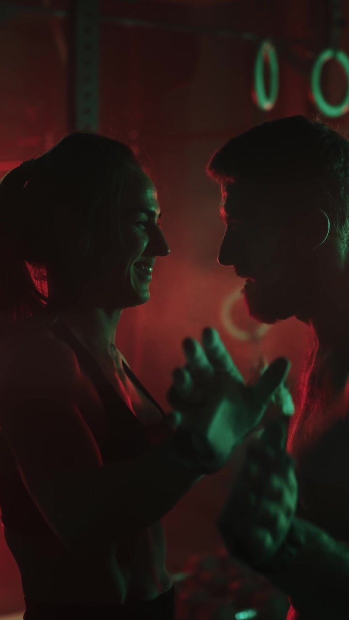 Uomo e donna muscolosi che si abbracciano dopo un allenamento intenso in una palestra illuminata al neon.