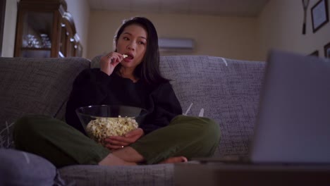 young asian woman sitting on sofa and eating popcorn