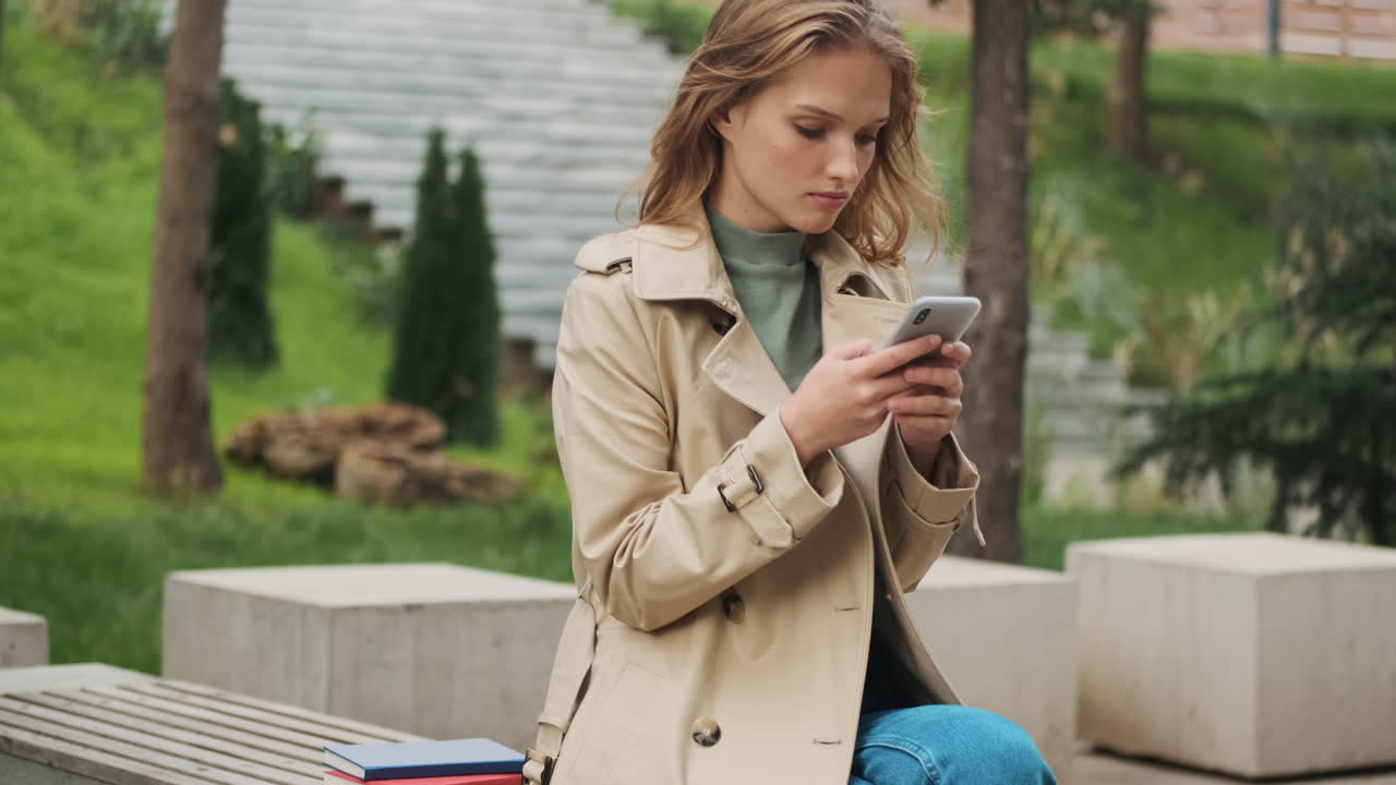 Caucasian female student with smartphone and books at the park.