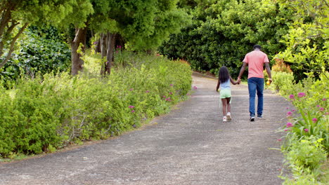 African American, Father and daughter walking hand in hand on garden path, enjoying nature, copy spa