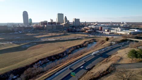 aerial-pullout-from-winston-salem-nc,-north-carolina-skyline-with-traffic-in-foreground