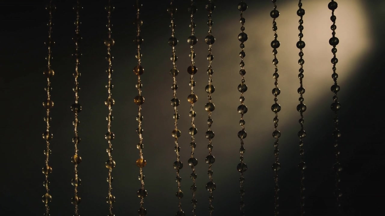 Shimmering beaded curtain bringing amber beads during focus shift, making warm bokeh in dim room