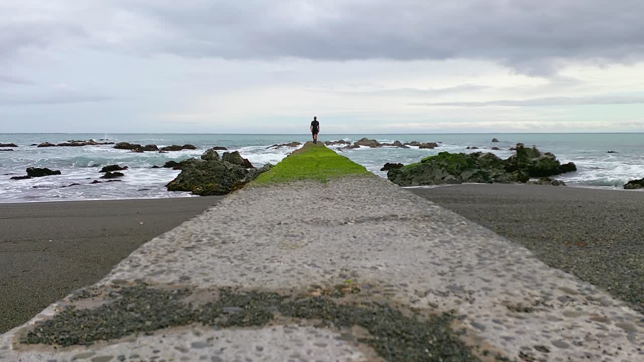 A man walking towards the camera from a platform over the ocean