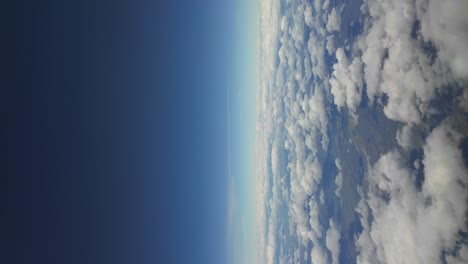 cloudscape over landscape, with a deep blue sky captured from above, shot from a jet cockpit